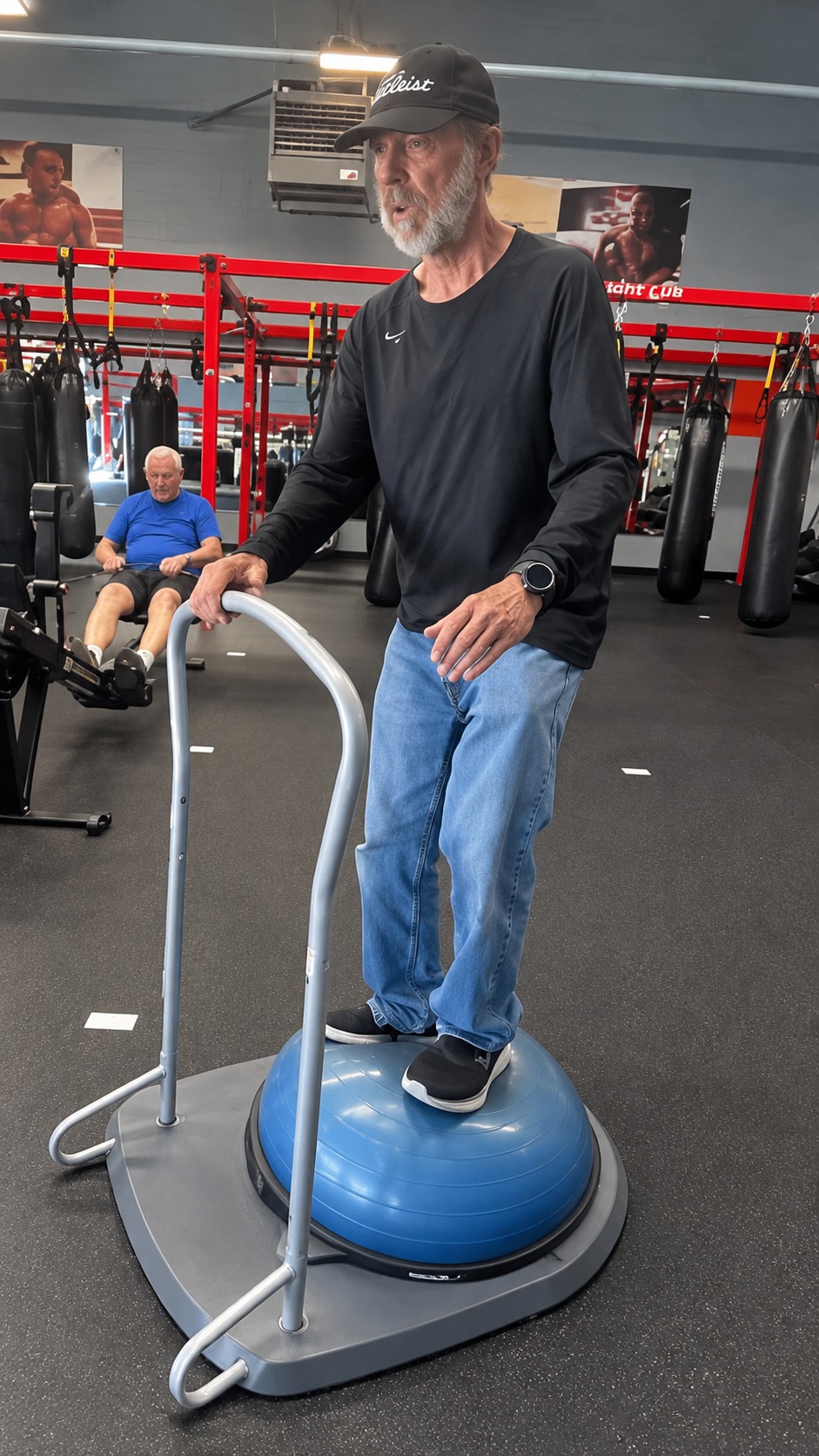 Senior member practicing balance on a blue balance trainer with a support rail